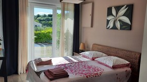 A bedroom with a bed, a bedside table with a plant, a view of greenery outside, and a painting on the wall. - Panoramic view Quiet private pool (Rasteau)