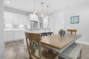 Una cocina moderna con armarios blancos, una mesa de comedor de madera y lámparas colgantes.