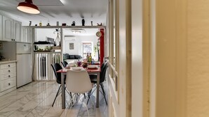 Une cuisine moderne avec des meubles blancs, un sol en marbre et un coin repas comprenant une table rouge et des chaises noires.