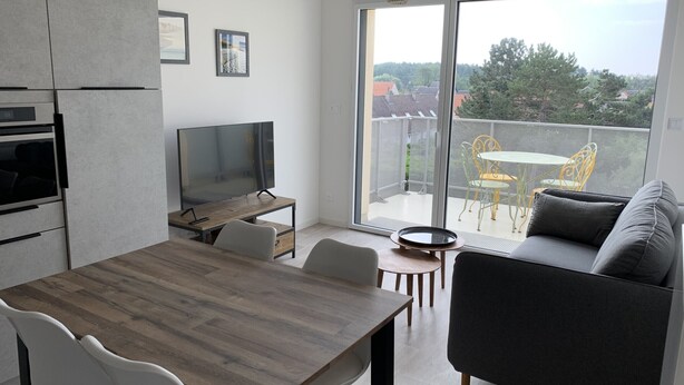 A modern kitchen with a dining area, a flat-screen TV, and a balcony with outdoor furniture. - Cozy 1BR Apartment in Central Fort-Mahon-Plage with Private Parking (Fort-Mahon-Plage)