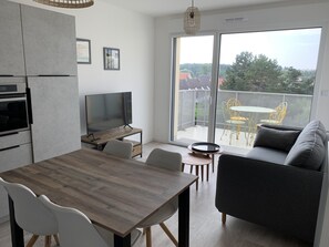 A modern kitchen with a dining area, a flat-screen TV, and a balcony with outdoor furniture. - Cozy 1BR Apartment in Central Fort-Mahon-Plage with Private Parking (Fort-Mahon-Plage)