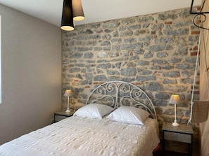Camera da letto con parete in pietra, struttura letto in metallo, biancheria bianca e due lampade da comodino.
