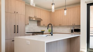 A modern kitchen with light wood cabinets, a central island with a sink, and pendant lighting. - Mountain Modern Condo Near Downtown (Ketchum)