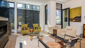 A modern living room with a glass coffee table, two armchairs, a sofa, and a fireplace. - Mountain Modern Condo Near Downtown (Ketchum)