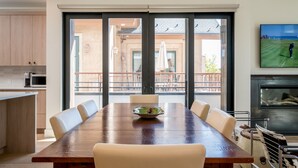 A dining area with a wooden table and beige chairs, a bowl of fruit, and a view of a balcony with outdoor furniture. - Mountain Modern Condo Near Downtown (Ketchum)