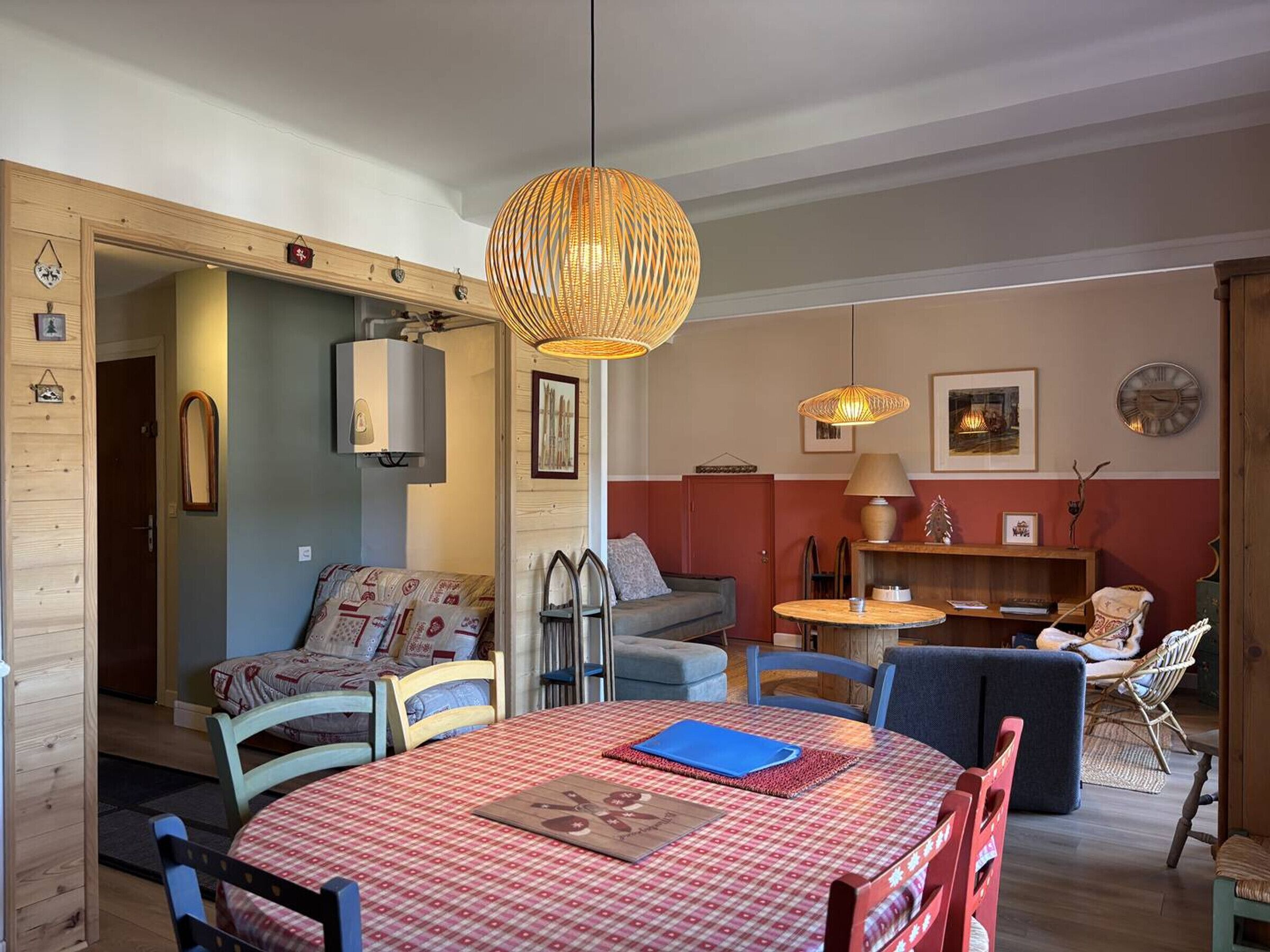 A cozy living room with a dining area, featuring a checkered tablecloth, wicker lamps, and a mix of modern and traditional decor.