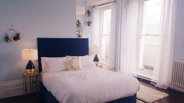 A bedroom with a large bed, two bedside tables, a wall-mounted lamp, and a window with sheer curtains. - The Bank Hotel & Bistro (St Leonards-On-Sea)