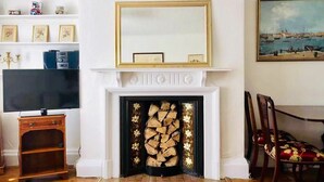 A living room with a fireplace, a television, and a dining area with chairs. - Entire Cottage Style Flat in Heart of Wallingford (Wallingford)