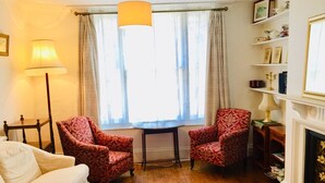 A cozy room with a wooden floor, two patterned armchairs, a white sofa, a small table, a lamp, and a fireplace. - Entire Cottage Style Flat in Heart of Wallingford (Wallingford)