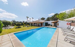 Une piscine rectangulaire entourée d’une terrasse carrelée, elle-même bord ée d’une pelouse bien entretenue et d’une petite maison dont le toit est également recouvert de tuiles.
