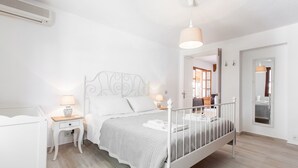Un dormitorio con una cama blanca, mesitas de noche, una lámpara colgante y suelo de madera.