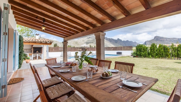 Un espacio al aire libre cubierto con comedor de madera, con mesa dispuesta para seis personas, rodeada de sillas acolchadas.