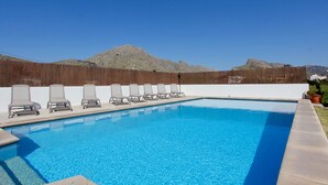 Una piscina rectangular con agua cristalina azul, rodeada por una cerca de madera y un muro blanco.
