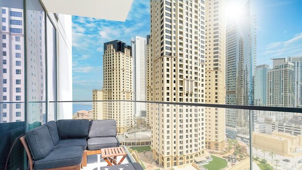 A modern living room with a sofa and coffee table, large windows offering a view of high-rise buildings.