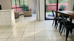 A spacious living area with a dining table, chairs, a sofa, and a kitchen area with cabinets.