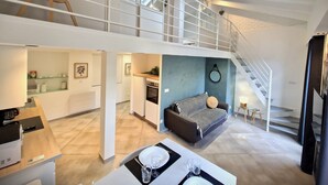 A spacious loft apartment with a mezzanine level, a kitchen, a dining area, and a living space with a sofa and a small table.
