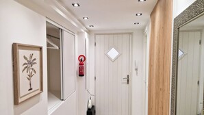 A hallway with a white door, a fire extinguisher mounted on the wall, and a framed picture on the left.