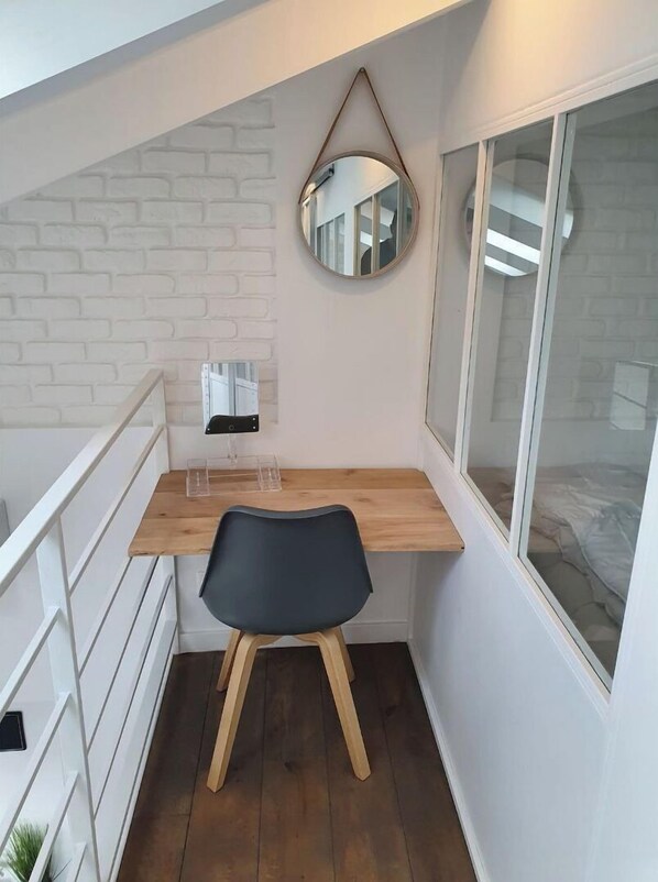 A small, modern room with a wooden desk, a black chair, a mirror, and a window.