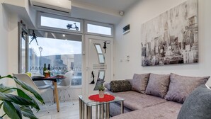 Una sala de estar moderna con una mesa de centro de vidrio, un sofá y un cuadro de un paisaje urbano en la pared.