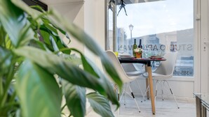Un comedor moderno con una mesa dispuesta para dos personas, una planta en maceta al frente y vistas de la ciudad a través de amplios ventanales.