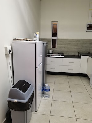 A compact kitchen with a refrigerator, a gas stove, and a trash bin. - Monument Park Lane (Gqeberha)