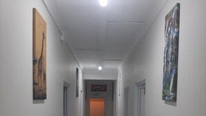 En gang med hvide vægge, flisegulv og kunst på væggene. Der er en udgangsskilte på væggen og en dør for enden af gangen.