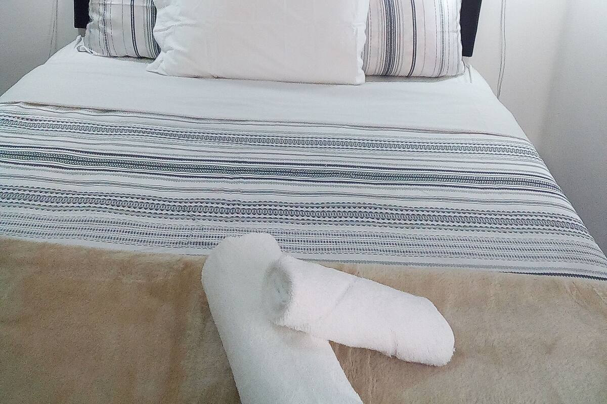 Ein Bett mit Kopfteil, Kissen, Decke und einem Handtuch auf dem Boden.