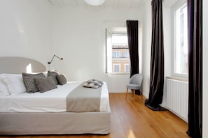 Ein Schlafzimmer mit Bett, Stuhl, Fenster und Blick auf Gebäude.