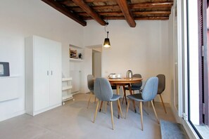 A dining area with a wooden table, four chairs, a hanging light fixture, a white cabinet, and a window with a view.