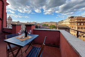 Ein Balkon mit Tisch, zwei Stühlen und einer Weinflasche.