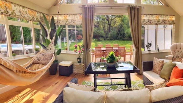 Een gezellige kamer met een hangmat, een bank, een tafel en uitzicht op een tuin en geparkeerde auto's.