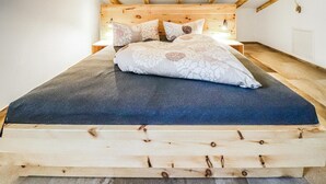 Een slaapkamer met een houten hoofdbord, een bed met beddengoed met een patroon, en een schuine plafond.