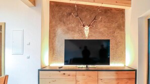 Een moderne woonkamer met een grote flatscreen televisie bevestigd aan een houten wand boven een kast met lades.