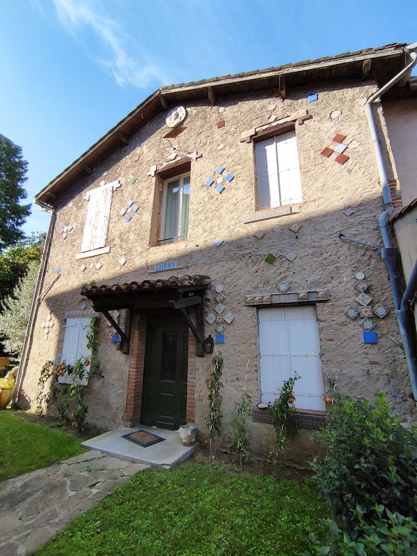 Uma vila rústica com porta verde, venezianas brancas e fachada de pedra.