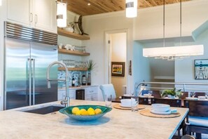 A modern kitchen with a stainless steel refrigerator, a bowl of lemons on the counter, and a dining area with a table set for two. - Private Pool-4 bikes-Private Beach Access (Santa Rosa Beach)