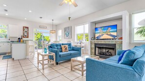 A spacious living room with a blue sofa, a coffee table, and a fireplace. There is a television mounted on the wall and a ceiling fan above. - Heated Pool, 4 BR,  Island Blessing, Beach Chairs, Short Walk to Beach (St. George Island)