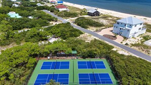 An aerial view of a coastal area with a tennis court, beach houses, and a large building. - Heated Pool, 4 BR,  Island Blessing, Beach Chairs, Short Walk to Beach (St. George Island)