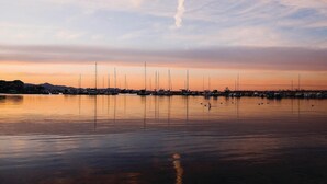En lysthavn med flere sejlbåde i havnen, roligt vand og en solnedgangshimmel.