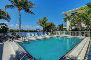 Une piscine entourée de chaises longues, de palmiers et d’un bâtiment doté de balcons.