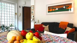 Un soggiorno con una tovaglia colorata e decorata, una ciotola di frutta e un quadro appeso al muro.