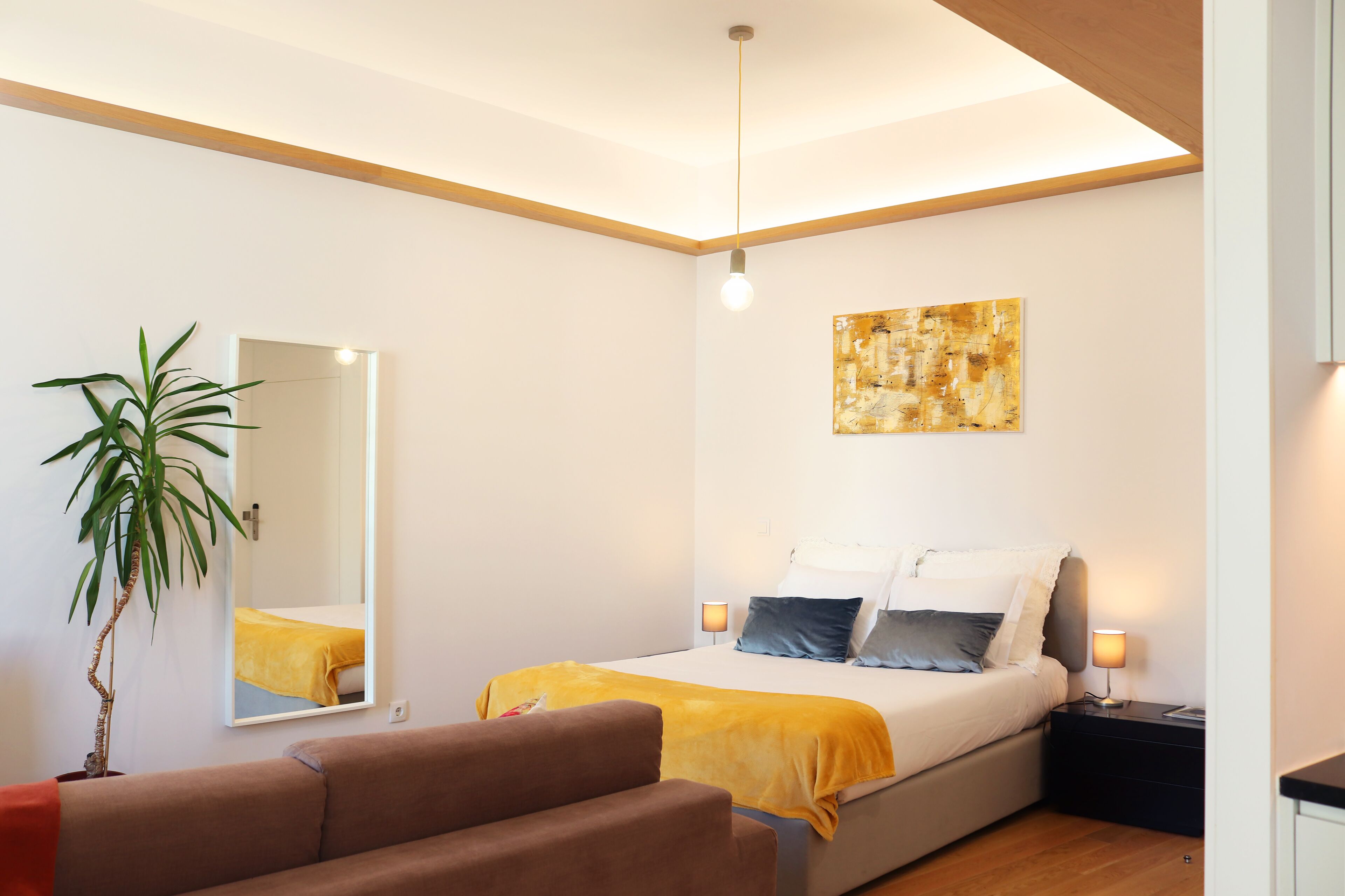 A modern bedroom with a bed, bedside lamps, a large mirror, and a painting on the wall.
