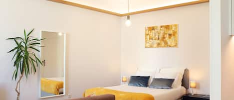 A modern bedroom with a bed, bedside lamps, a large mirror, and a painting on the wall.