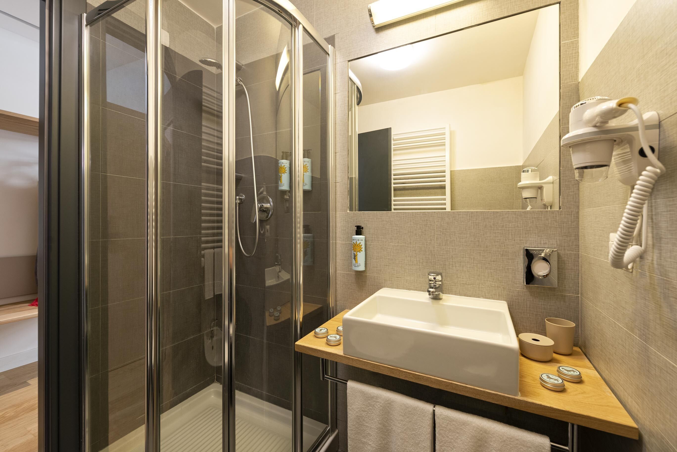 A modern bathroom with a glass-enclosed shower, a sink with a vanity, and a hairdryer mounted on the wall.