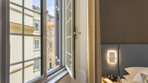 A hotel room with a large window, a bedside table with a camera and book, and a wall-mounted light. - Giuditta in Trastevere (Rome)