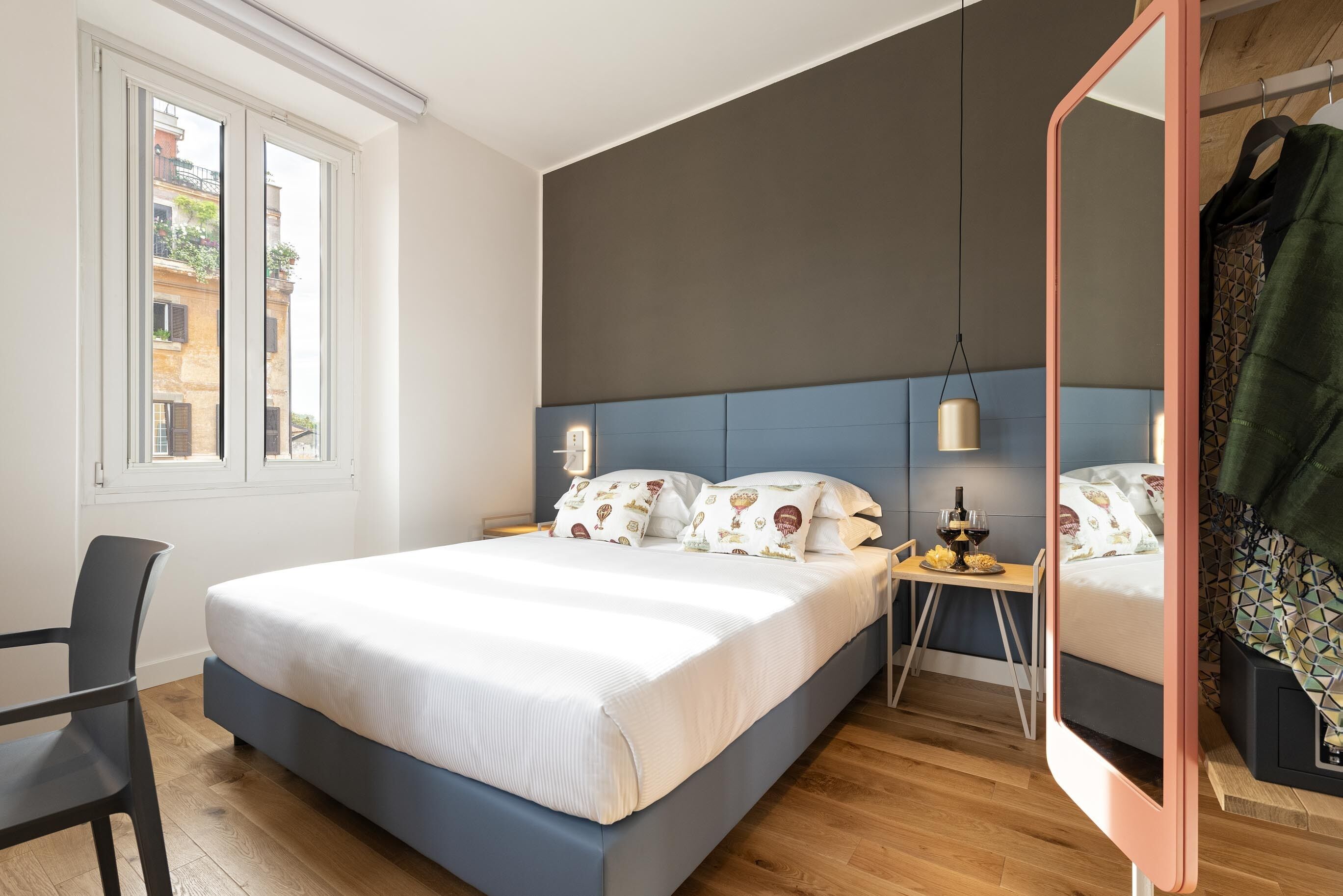 A modern bedroom with a large bed, bedside tables, a mirror, and a window with a view of buildings.
