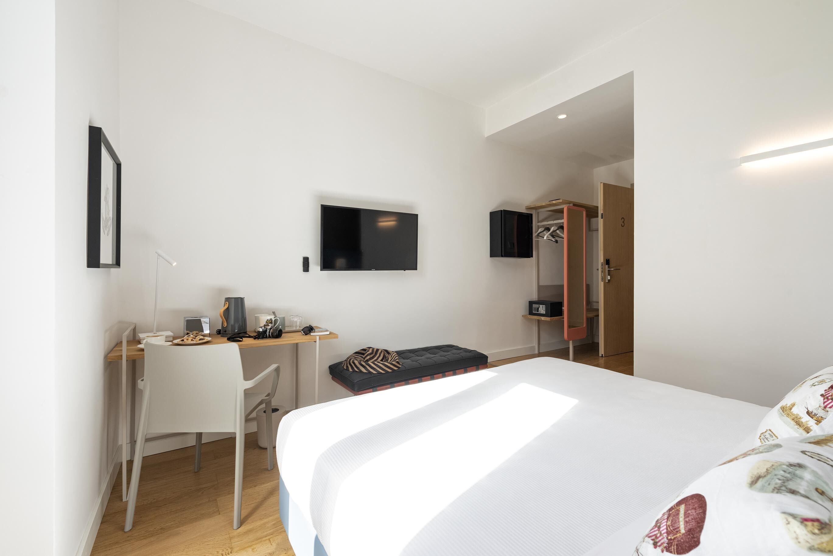 A modern hotel room with a bed, a desk, a chair, a TV, and a wardrobe.