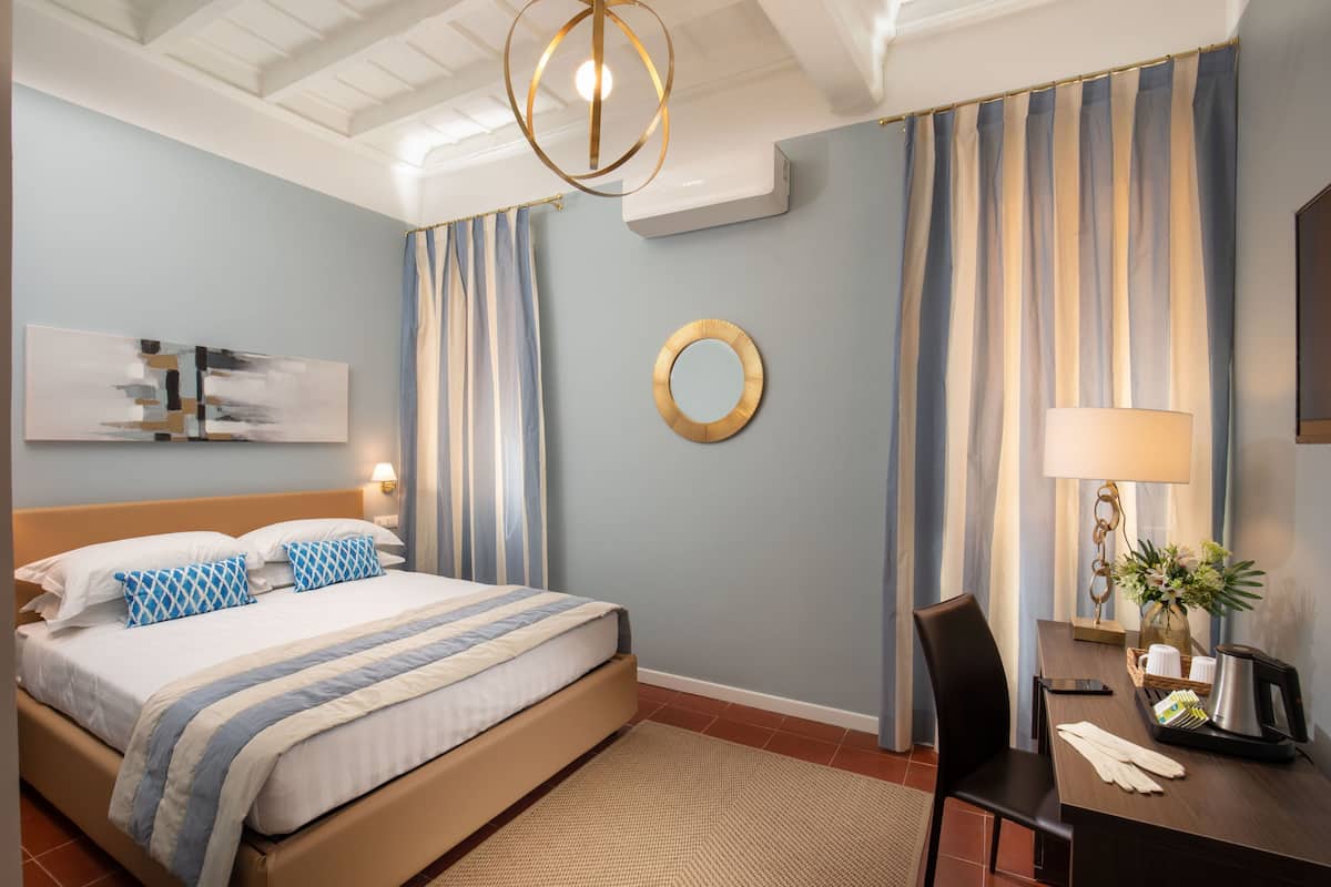 A hotel room with a bed, a desk, a lamp, and a vase with flowers.