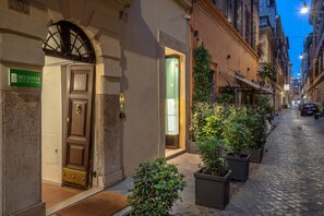 A narrow cobblestone street with a hotel entrance, a green sign, and potted plants lining the sidewalk. - Belsiana House (Rome)