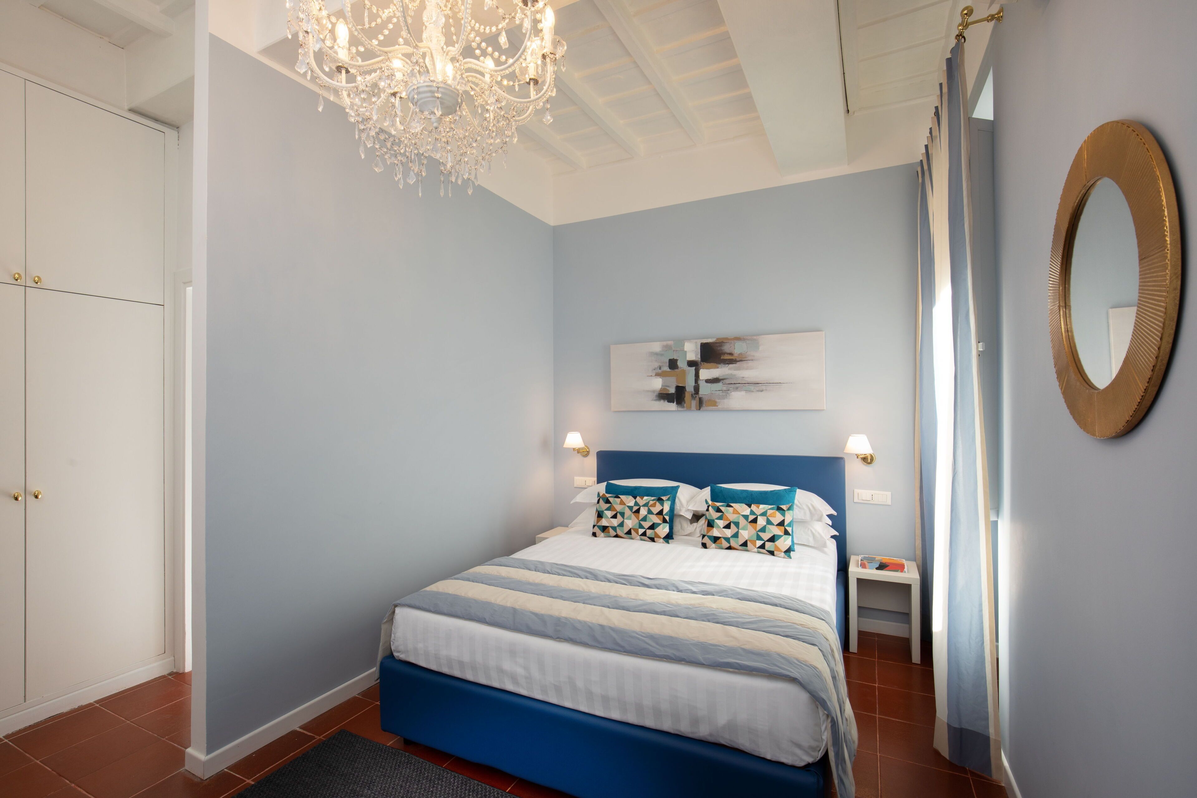 Un dormitorio con cama, candelabro, espejo en la pared y una puerta.