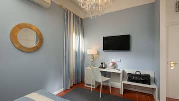 Una camera d'albergo con un letto, una scrivania con una sedia, una televisione, una lampada, una borsa e uno specchio.